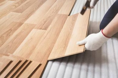 A person is installing a wooden floor with a hammer.