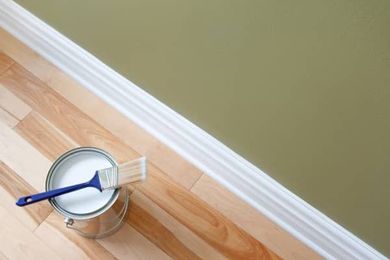 A can of paint and a brush on a wooden floor.